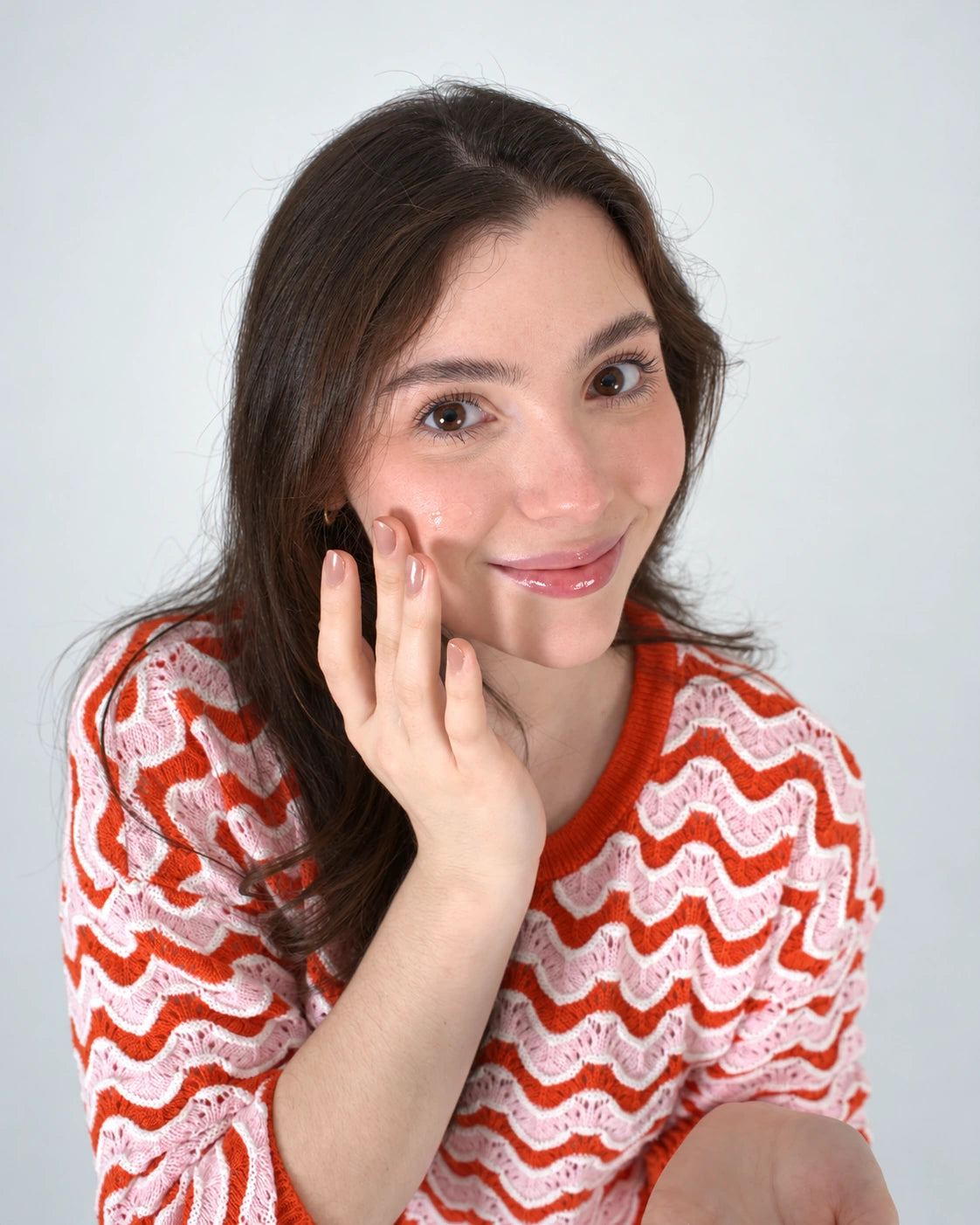 Modelo aplicando crema sobre la mejilla en su ritual de cuidado facial.